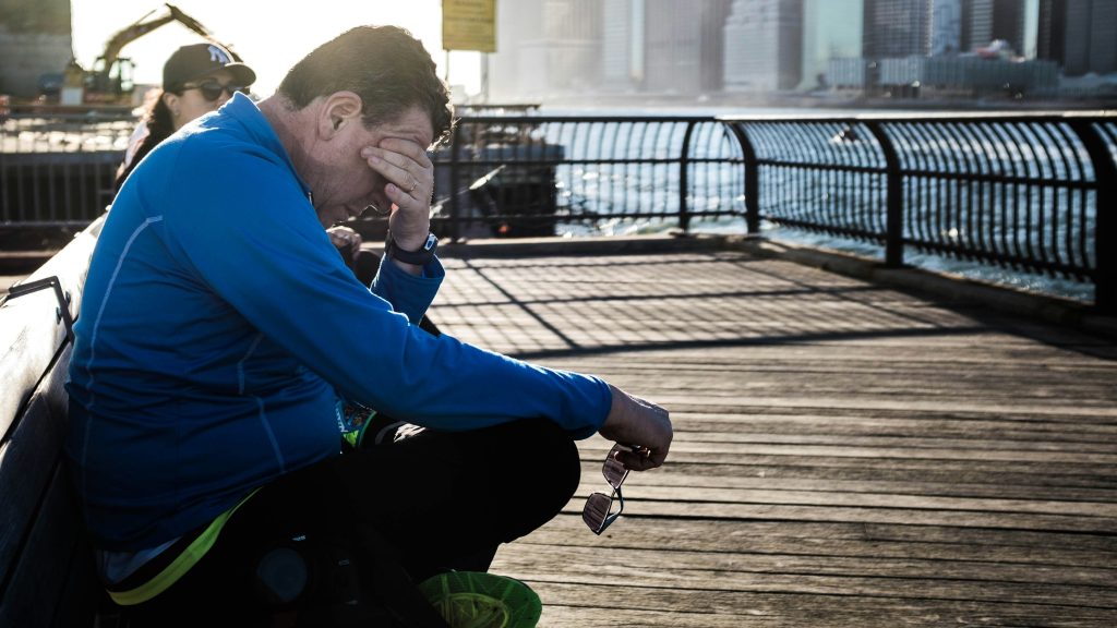 homme assis sur un banc qui se tient la tête