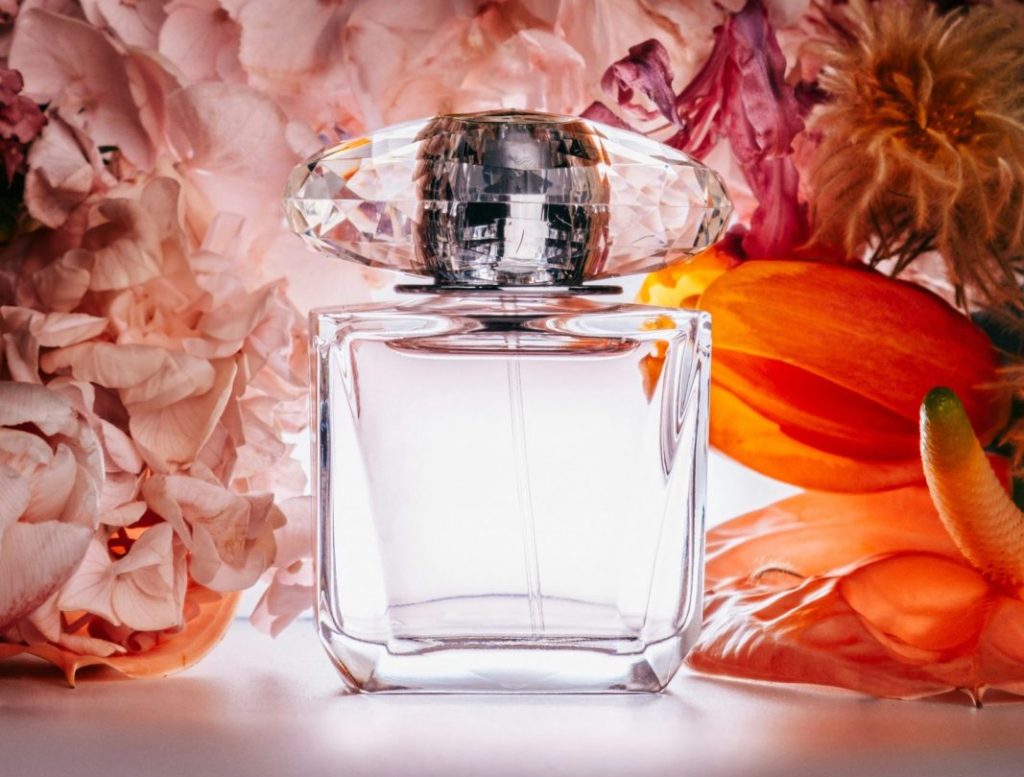 flacon de parfum vide transparent sur fond de fleurs rose et orange